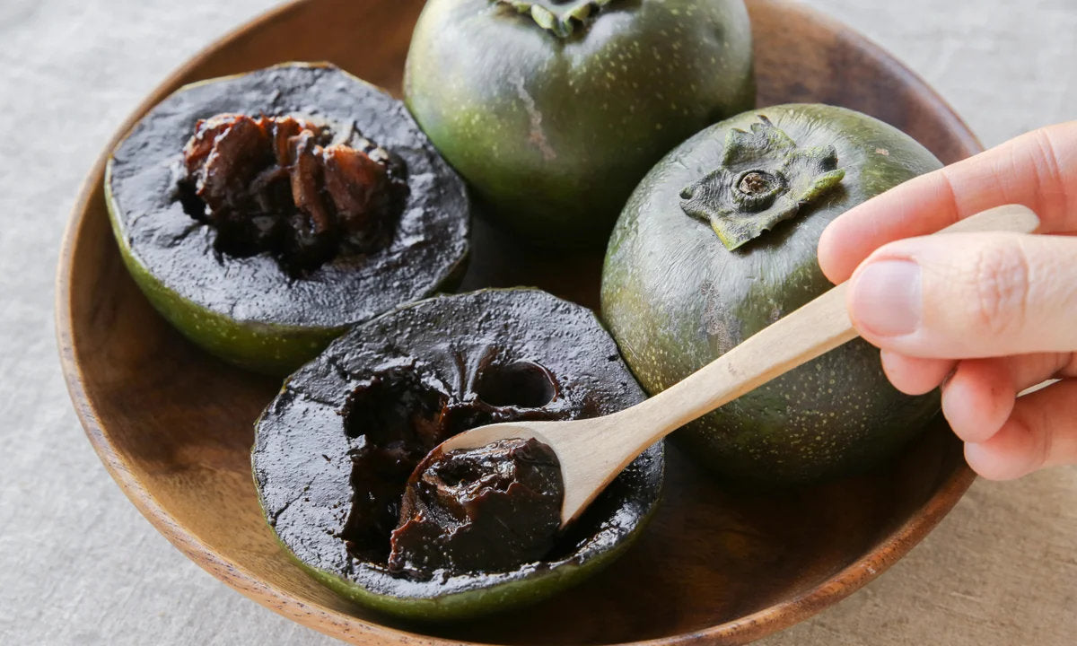 Chocolate pudding fruit, also known as black sapote, showing ripe dark brown flesh, green fruit skin, and glossy green leaves on a tropical fruit tree.