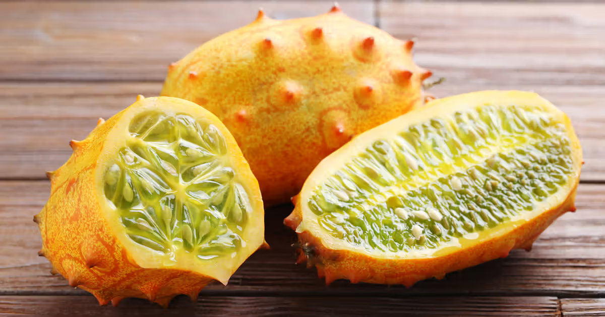 Jelly melon horned cucumber plant producing bright orange spiny fruits with juicy green flesh, growing on a leafy vine in a sunny home garden.
