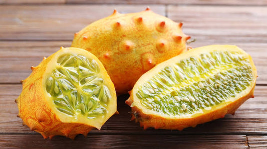 Jelly melon horned cucumber plant producing bright orange spiny fruits with juicy green flesh, growing on a leafy vine in a sunny home garden.