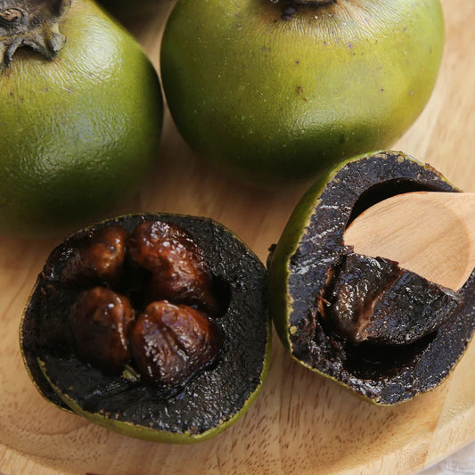 Chocolate pudding fruit, also known as black sapote, showing ripe dark brown flesh, green fruit skin, and glossy green leaves on a tropical fruit tree.