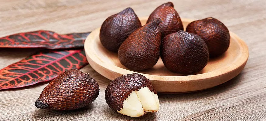 Salak fruit and salak palm showing reddish-brown scaly snake fruit, pale edible flesh, and long green tropical palm leaves.