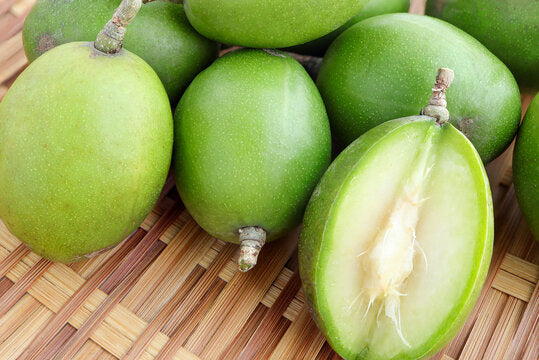 Ambarella Indian Hog Plum fruit tree with lush green compound leaves and clusters of oval green and golden-yellow fruits growing in a tropical garden.